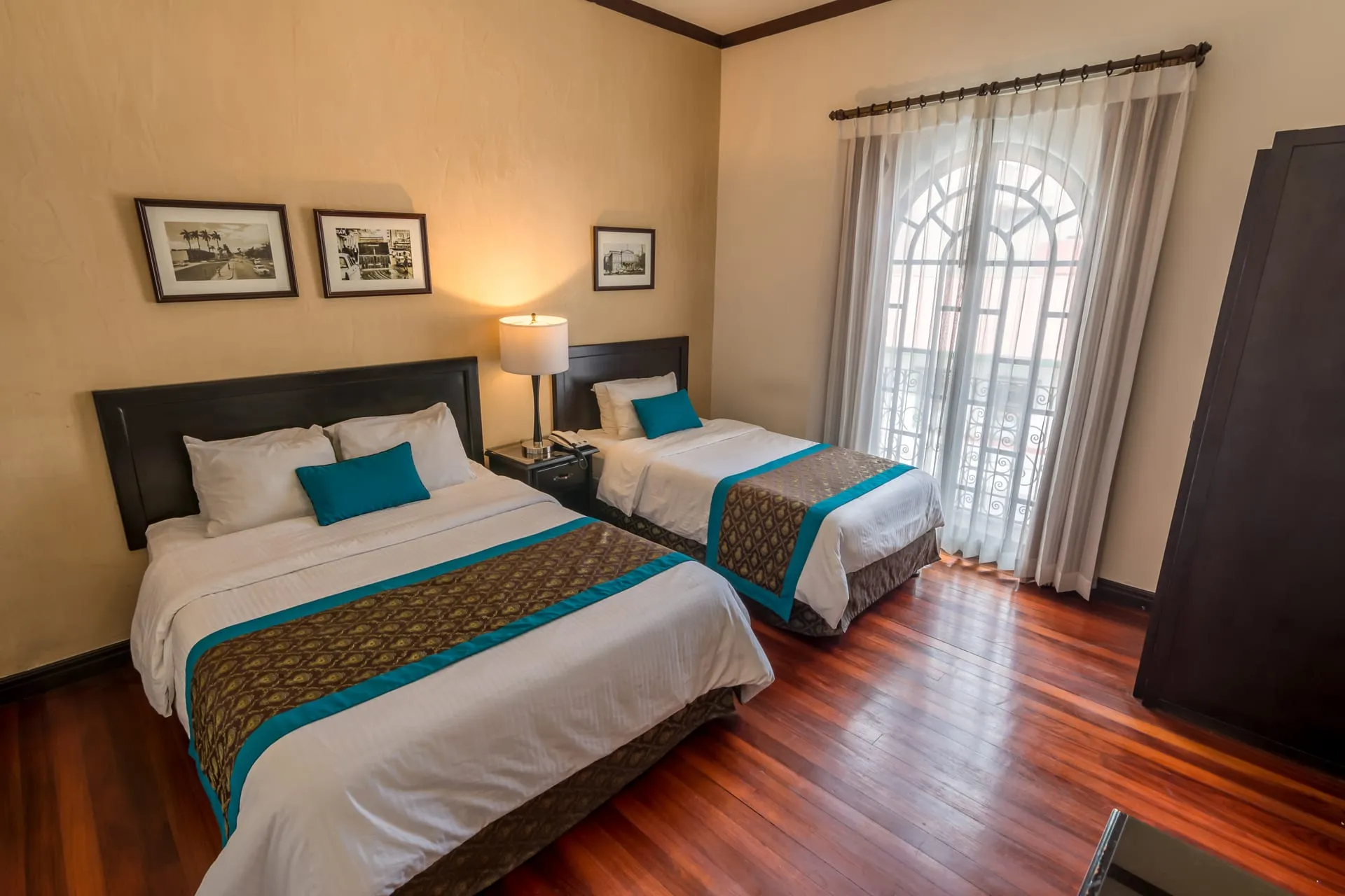 Habitación Triple con una cama doble y una individual, piso de madera y ventana arqueada con balcón de hierro forjado